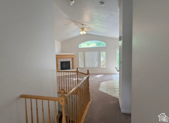 Vaulted ceilings, carpeted flooring, tile-accented fireplace with a wood mantel, arched window, and wooden staircase railing