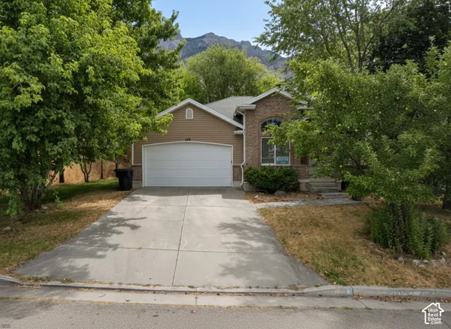 Single-story residence featuring a mixed brick and horizontal siding exterior, an arched window, a concrete driveway, and an attached two-car garage set against a mountain backdrop