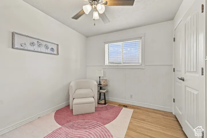 Interior space featuring wood-finish flooring, white beadboard wainscoting, a double-panel interior door, and a three-light ceiling fan with matching blade finish