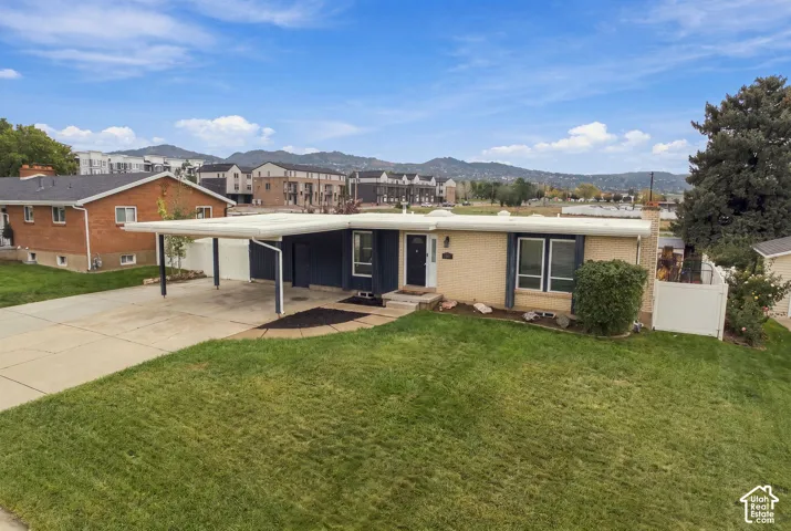 Single-story brick exterior residence featuring a flat roofline, attached carport, concrete driveway, and mountain backdrop