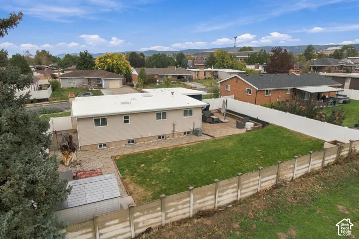 Fenced backyard featuring a manicured lawn, stone-paver patio, storage shed, and mature perimeter trees