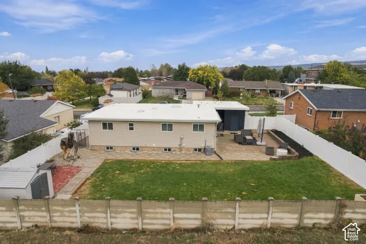Rear exterior featuring a large concrete patio, manicured lawn, white vinyl fencing, and a detached storage structure