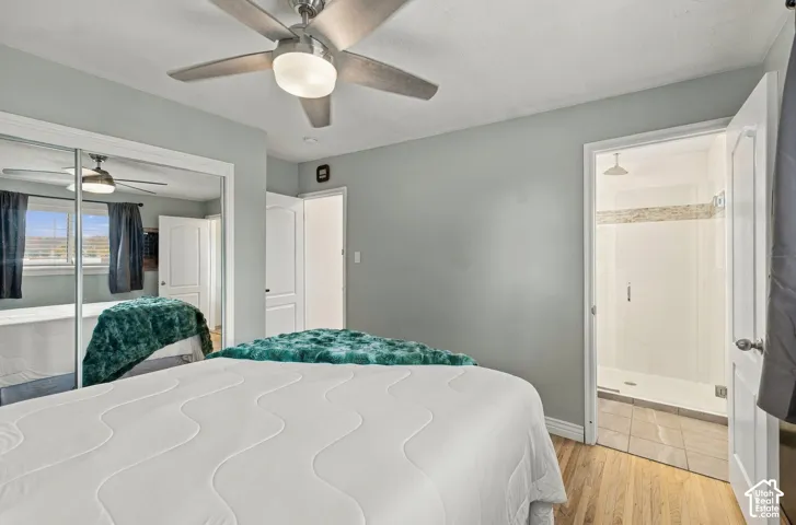 Bedroom featuring wood-finish flooring, a ceiling fan with integrated lighting, mirrored sliding closet doors, and an attached bathroom with a tiled walk-in shower