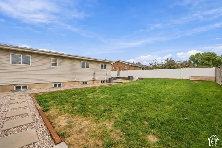 Private backyard featuring a grass lawn, gravel path with concrete pavers, and a full-perimeter white vinyl privacy fence