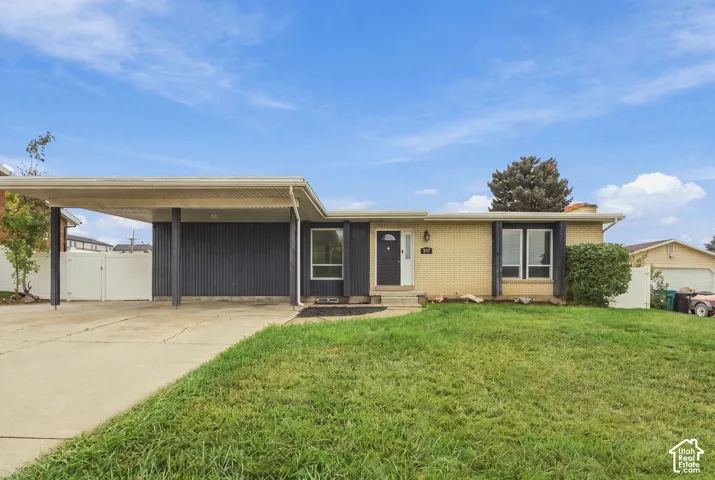 Mid-century ranch exterior featuring light-toned brick masonry, a covered carport with vertical siding, and multiple picture windows