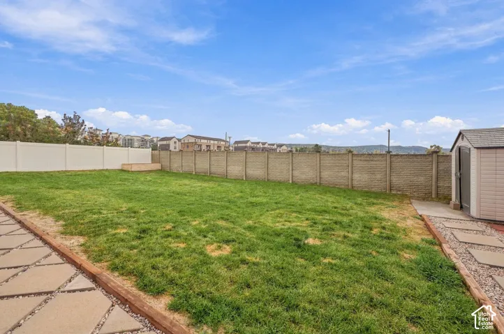 Expansive backyard featuring a lawn, perimeter fencing, concrete paver walkways, and a detached storage shed
