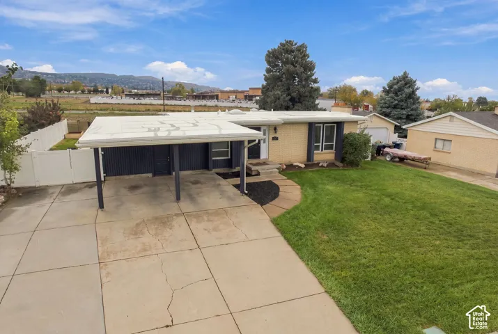 Single-story residence featuring light brick exterior, covered carport, concrete driveway, and expansive lawn area