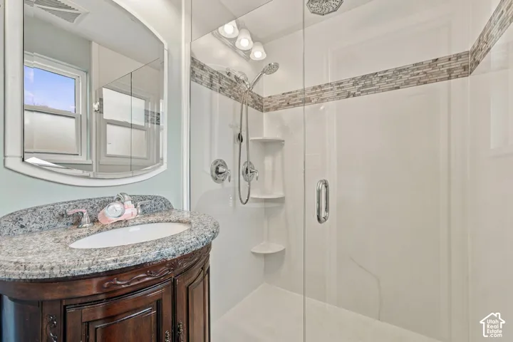 Bathroom vanity with stone-finish countertop and integrated sink, frameless glass shower enclosure, built-in shelving, decorative tile inlay, and chrome finish hardware