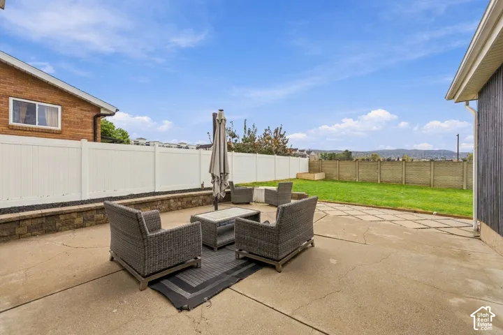 Private backyard featuring a concrete patio, stone-block retaining wall, vinyl perimeter fencing, and open lawn area