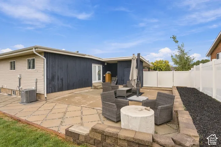 Rear patio featuring custom geometric concrete pavers, stacked stone retaining wall, and full-height white vinyl privacy fencing