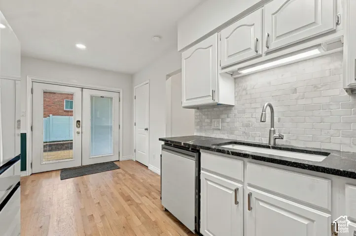 Kitchen featuring white cabinetry, dark stone-finish countertops, a light-toned brick-pattern backsplash, a stainless steel gooseneck faucet, and wood-finish flooring