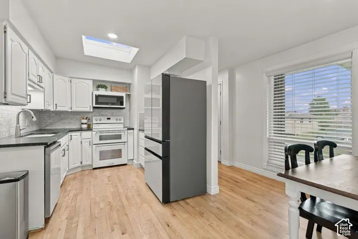 Kitchen featuring white cabinetry, wood-finish flooring, a ceiling skylight, tiled backsplash, and stainless steel appliances