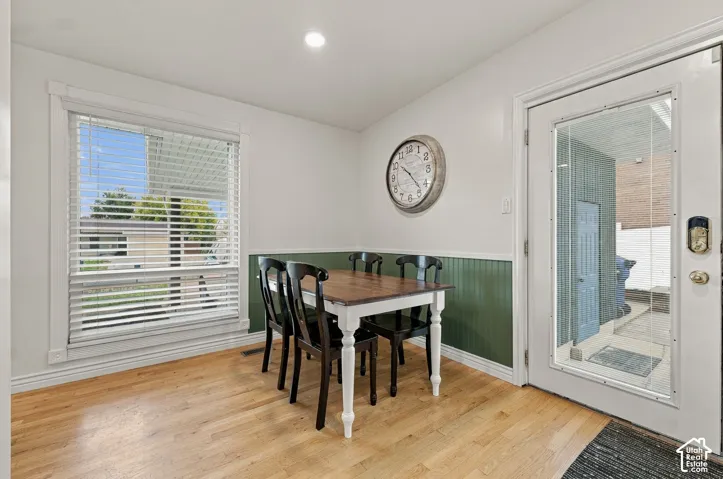 Wood-finish flooring, half-wall beadboard paneling, large picture window with blinds, and exterior entry door with integrated glass pane