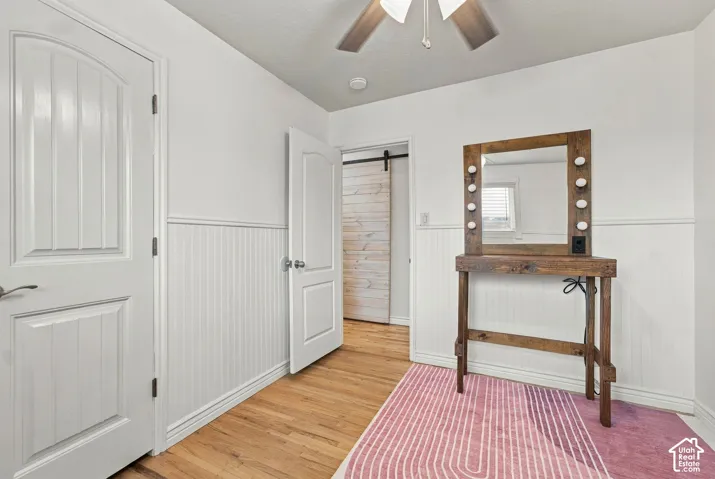 Room featuring wood-finish flooring, white beadboard wainscoting, two-panel interior doors, and a sliding barn-style door