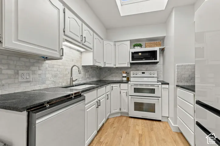 Kitchen featuring white cabinetry, dark stone-finish countertops, brick-pattern backsplash, wood-finish flooring, and a skylight