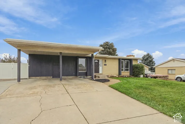 Single-story exterior featuring a brick facade, vertical siding, attached carport, and concrete driveway