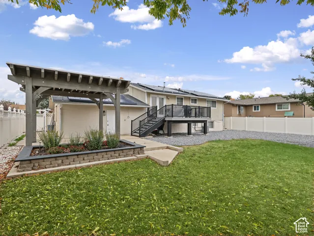 Backyard featuring a custom pergola, raised stone planter, elevated deck with black metal railing, solar panels, and perimeter privacy fencing