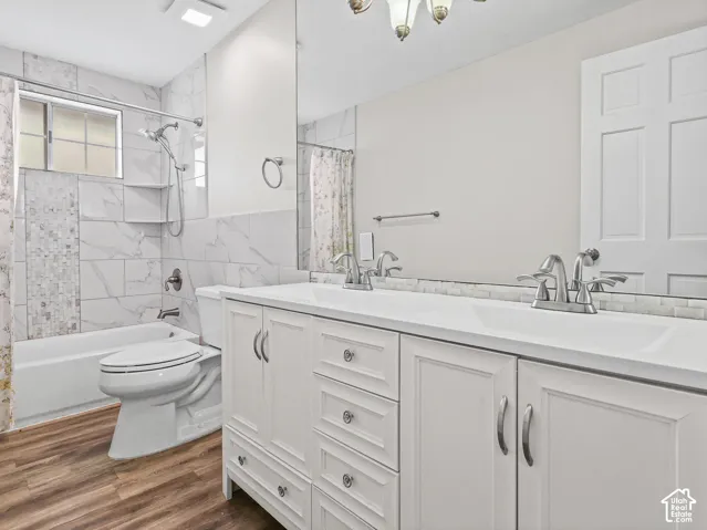 White vanity with a double-sink configuration, large wall-mounted mirror, wood-finish flooring, and a bathtub surround featuring patterned tile accents
