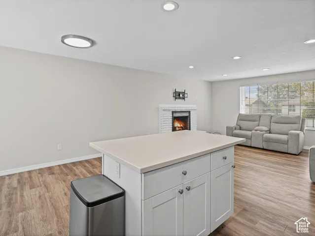 Kitchen island with solid-surface countertop and white cabinetry, recessed lighting, wood-finish flooring, and a fireplace with a white painted brick surround