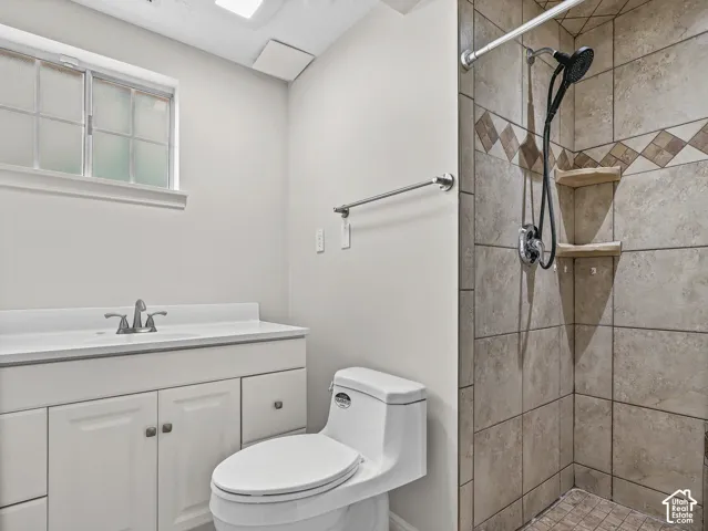 White vanity with integrated sink, tiled walk-in shower with decorative inlay, built-in shelving, and frosted-glass window