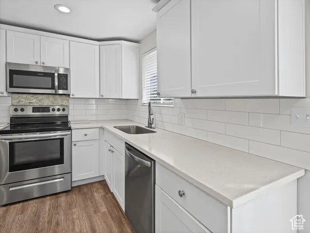 Kitchen featuring white shaker-style cabinetry, solid surface countertops, a white subway tile backsplash, stainless steel appliances, and wood-finish flooring