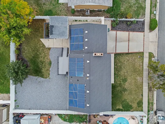 Aerial perspective featuring a roof-mounted solar array, a gray composite deck with stairs, a gravel-surfaced yard area, and a concrete driveway with brick trim accents