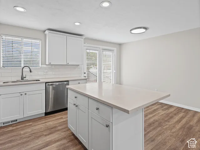 Kitchen featuring white cabinetry, quartz countertops, a central island with storage, stainless steel dishwasher, and wood-finish flooring
