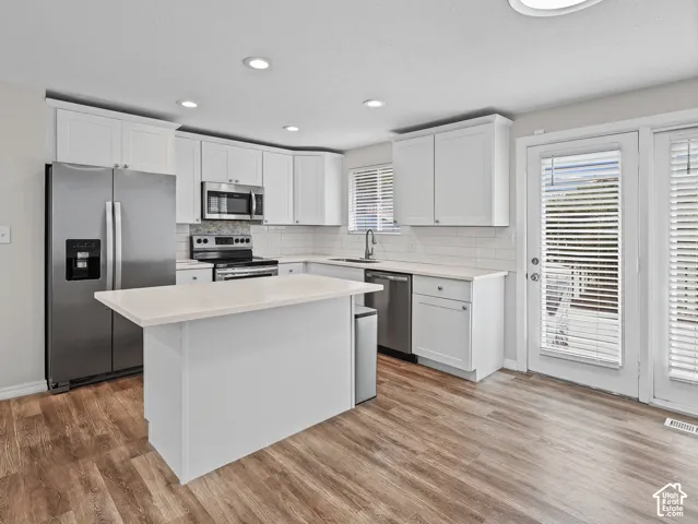 Kitchen featuring white shaker-style cabinetry, quartz countertops, subway tile backsplash, stainless steel appliances, and wood-finish flooring