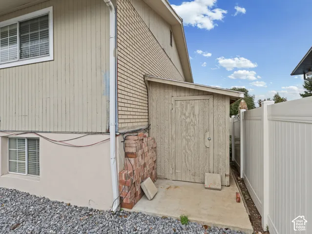 Exterior features include vertical wood-composite siding, a brick facade section, a concrete utility shed with a shed roof, and a perimeter vinyl privacy fence