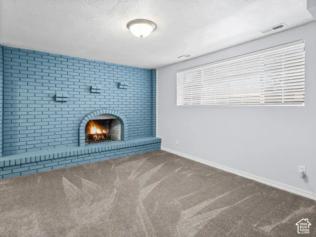 Painted brick wall featuring an arched fireplace and built-in hearth, paired with wall-to-wall carpeting and horizontal blinds