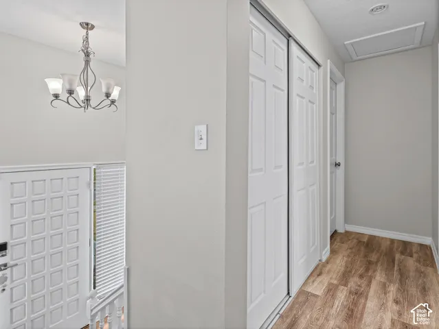 Hallway featuring wood-finish flooring, a multi-arm chandelier with frosted glass shades, a closet with six-panel sliding doors, and a paneled entry door with sidelight blinds