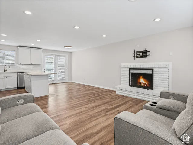 Open-concept interior featuring wood-finish flooring, recessed lighting, a painted brick fireplace, white cabinetry, and double glass doors