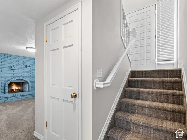 Interior entry featuring a carpeted staircase with a white handrail, a paneled door, and a brick fireplace surround