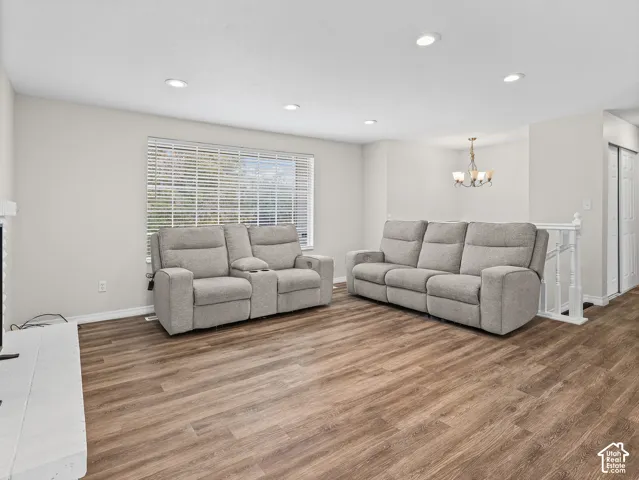 Living area featuring wood-finish flooring, recessed lighting, a multi-bulb chandelier, a large window with blinds, and a white painted fireplace surround
