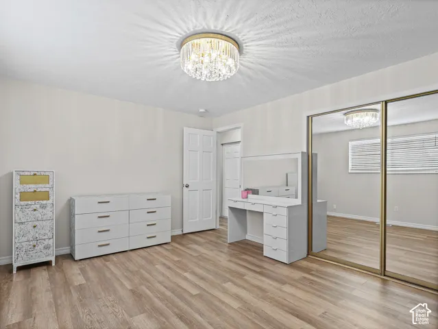 Room featuring wood-finish flooring, a tiered crystal flush-mount light fixture, and floor-to-ceiling sliding mirrored closet doors with gold-tone frames