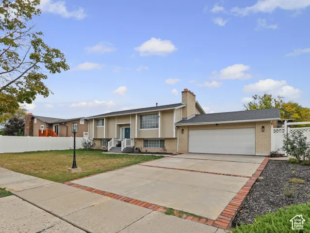 Split-level exterior featuring a brick and siding facade, attached two-car garage, concrete driveway with brick inlay, and white vinyl privacy fencing