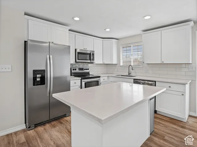 Kitchen featuring white shaker cabinetry, stainless steel appliances, light-toned stone-finish countertops, subway tile backsplash, and wood-finish flooring