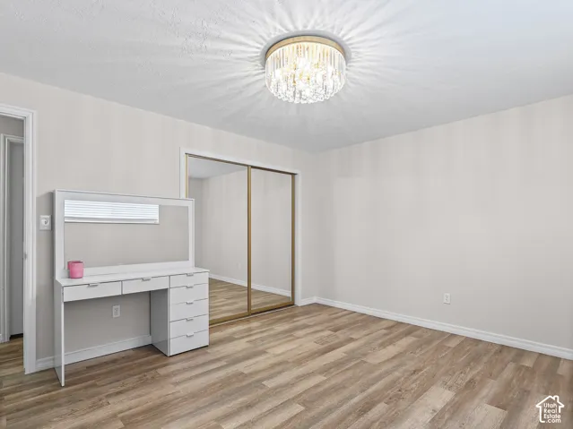 Wood-finish flooring, ceiling-mounted crystal-style flush mount light fixture, and floor-to-ceiling mirrored sliding closet doors
