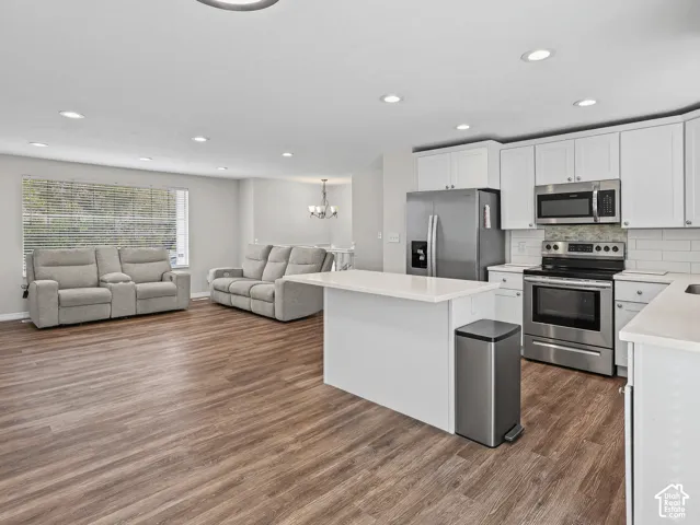 Open-concept kitchen featuring white shaker-style cabinetry, quartz countertops, a central island, and stainless steel appliances, set against wood-finish flooring and recessed lighting