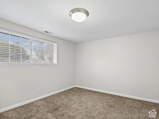 Neutral-toned interior space featuring wall-to-wall carpeting, a large window with horizontal blinds, and a brushed-nickel flush-mount ceiling light fixture