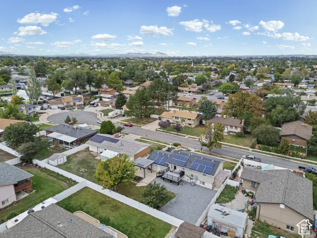 Aerial perspective featuring a residential property with roof-mounted solar panels, an elevated rear deck, a paved patio area, and a white privacy fence enclosing the backyard