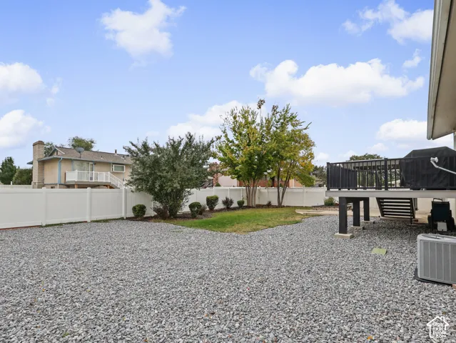 Backyard featuring a raised deck with black railing, white privacy fencing, gravel ground cover, and a central lawn area with mature trees