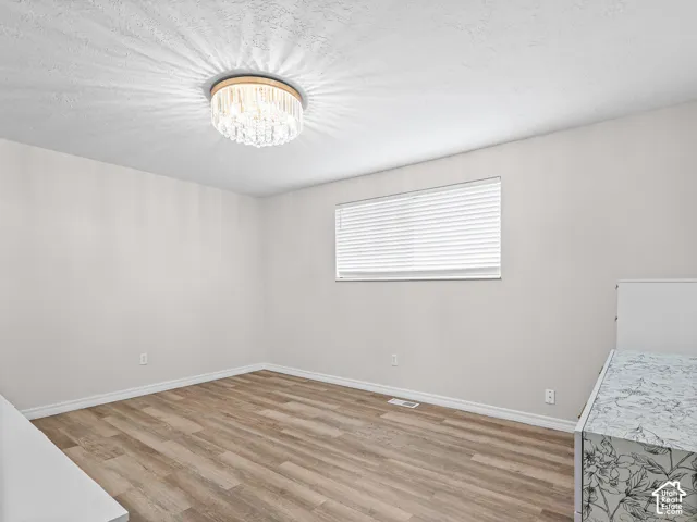 Room featuring wood-finish flooring, a tiered crystal flush-mount light fixture, and horizontal window blinds