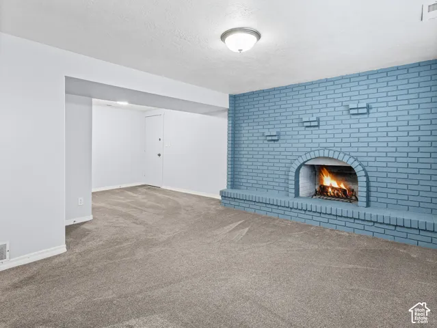 Painted brick accent wall featuring an arched fireplace hearth, carpeted flooring, and a flush-mount ceiling light fixture