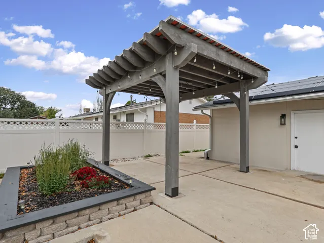 Concrete patio featuring a timber pergola, raised garden bed with stone masonry, and white vinyl privacy fencing