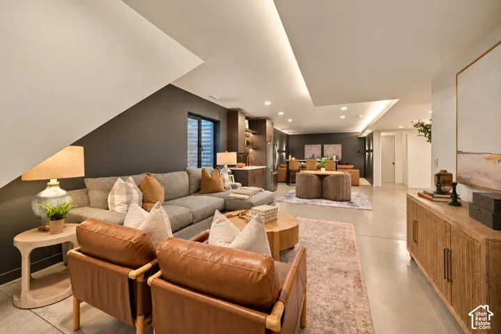 Open-concept interior featuring polished concrete flooring, recessed lighting, architectural soffit with integrated cove lighting, and a built-in wet bar with dark cabinetry