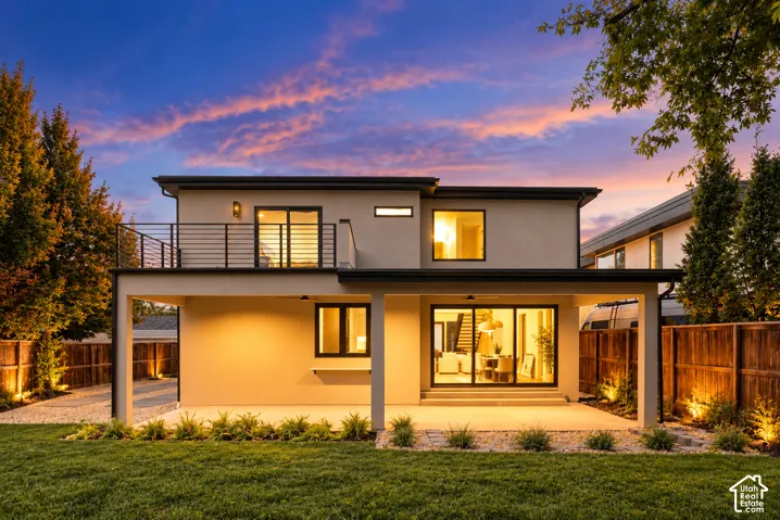 Stucco exterior featuring an upper-level balcony with metal railing, a covered ground-floor patio, sliding glass doors, and a wood privacy fence