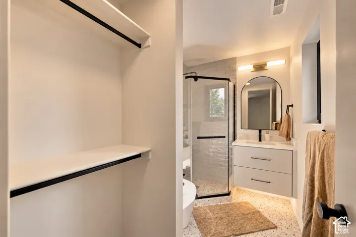 Floating vanity featuring a stone-surface countertop, arched wall mirror, matte black fixtures, corner shower with glass enclosure, and built-in closet shelving