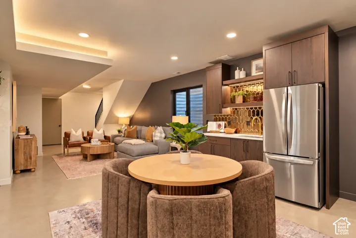 Kitchenette featuring dark wood cabinetry, a metallic honeycomb-patterned backsplash, light-colored countertops, recessed ceiling lighting, and polished concrete flooring