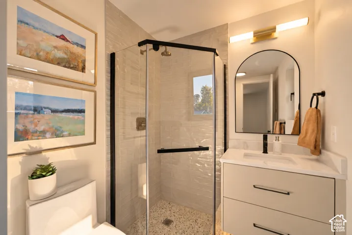 Corner shower enclosure with textured tile walls, floating vanity with a stone countertop, integrated sink, arched mirror, and brass-tone wall-mounted lighting
